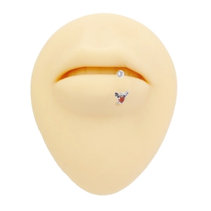 Detailed view of silver wing piercing with red heart gemstone on silicone lip model