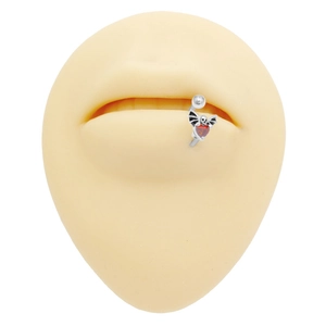 Dettaglio di piercing labret gotico in argento con cuore rosso e ali di pipistrello