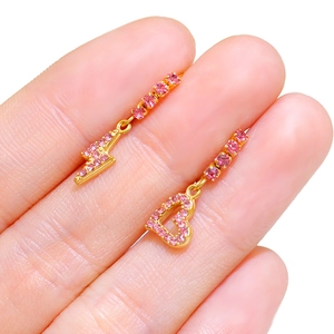 Dettaglio di orecchini asimmetrici placcati oro con ciondoli a cuore e fulmine in strass rosa