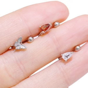Macro shot of steel piercing jewelry with orange zircon, clear zircon and opal butterfly charm