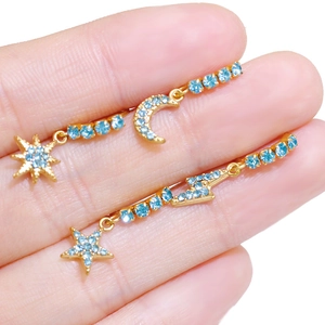 Gold lightning and star moon earrings set with light blue rhinestones on a finger