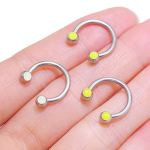 Three-piece titanium horseshoe nipple rings with yellow circular insets held in a hand