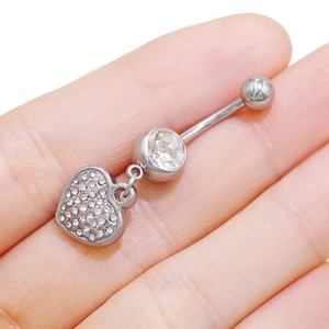 Primer plano de un piercing para el ombligo con forma de corazón plateado y circonitas