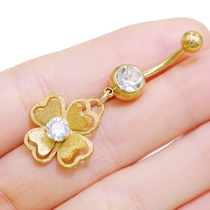 Detalle macro de piercing de ombligo de trébol dorado con pétalos de cristal