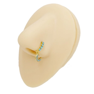 Detailed view of a gold nose ring with blue rhinestones and a moon pendant on a model