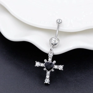 Macro shot of curved belly ring with cross pendant and black heart-shaped gemstone