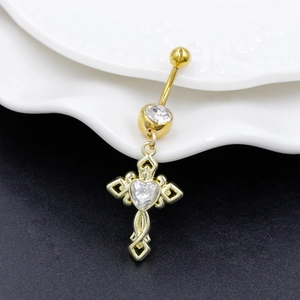 Detail of gold cross belly ring with heart-shaped zircon on a white textured plate