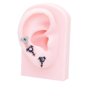 Macro detail of bat wing ear studs with eyeball and cross pendants on ear model