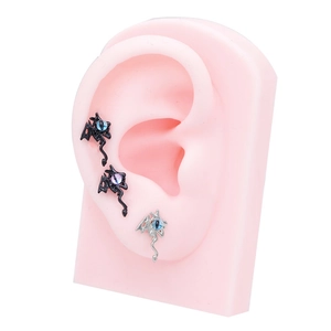Gothic dragon ear studs with blue and purple gemstones on pink silicone ear model