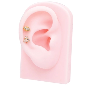 Detailed shot of gold-tone evil eye and fan-shaped stud earrings on a pink ear model