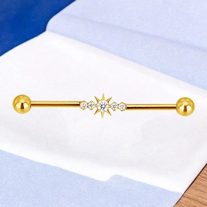 Detailopname van gouden industriële piercing met zonnestraal ontwerp en witte kristallen