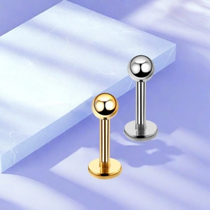 Polished F136 titanium flat back stud earrings in gold and silver on a marble base