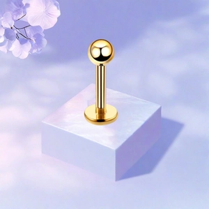 Macro view of golden F136 titanium labret stud with a polished ball on a white marble base