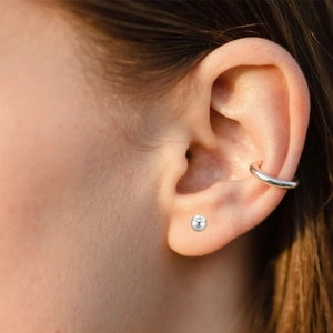 Detailed close-up of F136 titanium piercing stud and polished cuff earring on ear