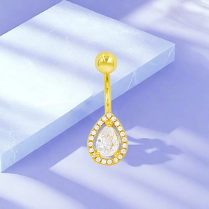 Detalle de piercing para ombligo dorado con circonita pera en soporte de mármol