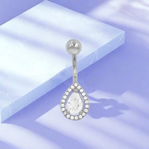 Detalle de piercing de ombligo plateado con circonita de gota sobre base de mármol