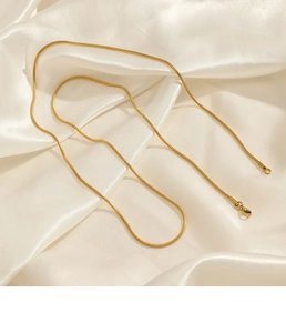 Détail d'un collier chaîne serpent dorée avec fermoir homard sur satin blanc doux