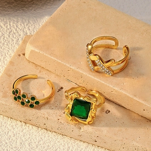 Detailaufnahme von drei vergoldeten Ringen mit grünem Smaragd und Buchstabe A auf Steinsockel