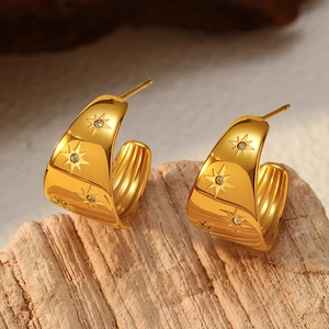 Détail macro de boucles d'oreilles dorées en C avec étoiles gravées et pierres de zircon