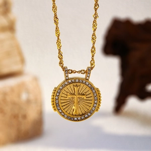 Détail d'un collier pendentif croix doré orné de strass brillants sur chaîne ondulée