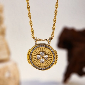 Détail macro d'un pendentif rond doré avec motif trèfle à quatre cœurs en zircons brillants