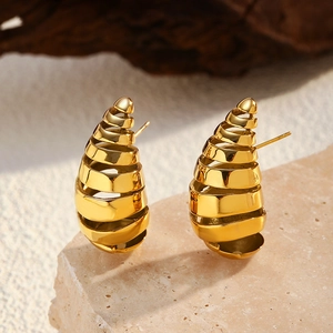Detalle de pendientes de gota huecos en espiral dorados sobre soporte de piedra natural