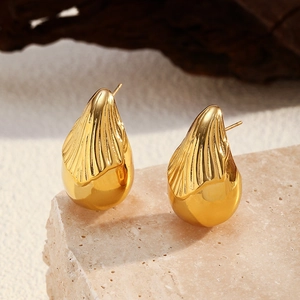 Detalle de pendientes de gota bañados en oro de 18K con textura de concha sobre mármol
