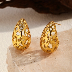 Detalle de pendientes de gota dorados con diseño de malla irregular sobre piedra