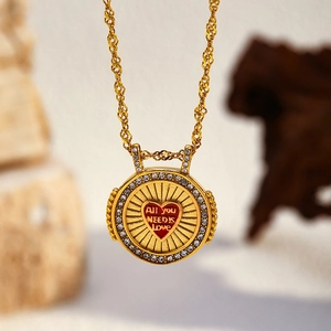 Détail macro du collier doré avec pendentif cœur et gravure All You Need Is Love élégante