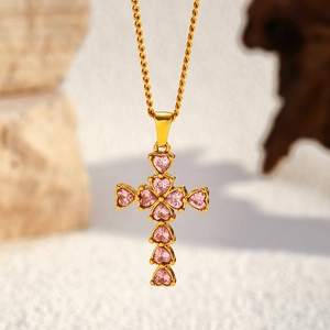 Close-up of pink heart gemstones inlay on gold cross pendant with rope chain