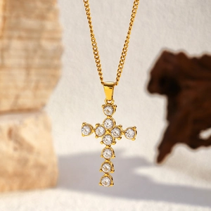 Close-up of gold cross pendant with round zircons on a rustic stone background