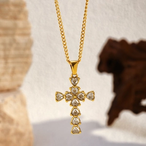 Macro view of 18K gold plated cross pendant necklace with heart-cut crystals on wood