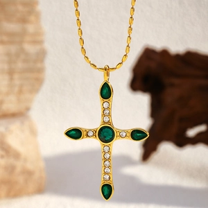 Close-up of gold cross pendant with green emeralds and small white diamonds on bead chain