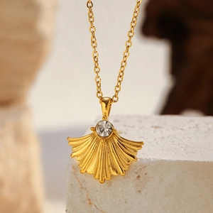 Vue détaillée du pendentif feuille de ginkgo dorée avec cristal sur support en pierre
