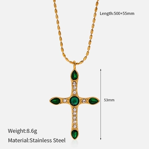 Macro detail of a gold stainless steel cross pendant with green pear-shaped gemstones