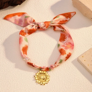 Floral print silk scarf necklace featuring a gold sunflower pendant on a textured base