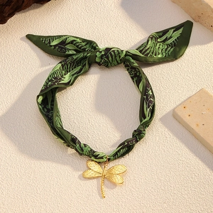 Detailed close-up of a golden dragonfly pendant on a dark green botanical silk scarf