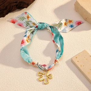 Close-up of sky blue floral silk scarf with golden flower pendant on textured stone
