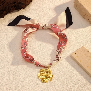Close-up of printed silk ribbon choker with a textured gold flower pendant on stone base