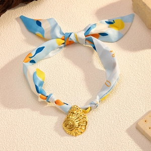 Detail of blue silk scarf necklace with a golden sea shell pendant on a sandy surface