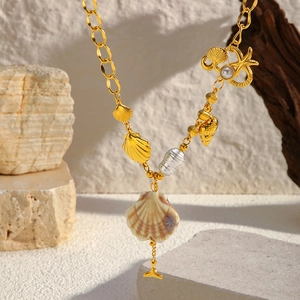 Détail des breloques coquillage et étoile de mer sur un collier doré à maillons
