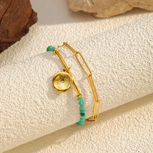 Detail of double-layer gold chain bracelet with green beads and sunburst pendant charm