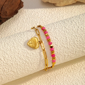 Macro detail of double-layer bracelet with pink beads and golden heart eye pendant