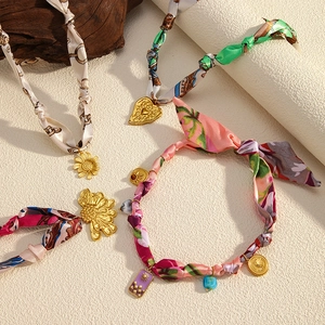 Macro shot of printed silk scrunchies with various gold metal charms on stone background