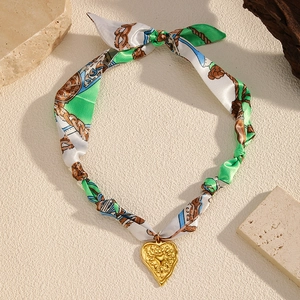 Macro shot of a vintage gold heart pendant with textured green and white silk scarf chain