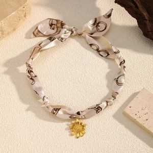 Detail of silk scarf choker with gold sunflower pendant on a natural stone background