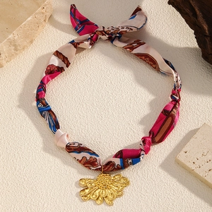 Detailed macro view of a silk scarf necklace with a golden daisy charm accessory