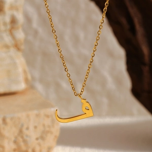Gros plan d'un pendentif en or 18 carats avec lettre arabe sur chaîne en acier inoxydable