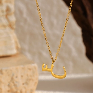 Gros plan d'un pendentif lettre arabe en or 18k avec chaîne fine sur socle en pierre