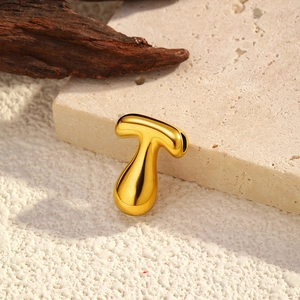 Macro shot of polished gold letter T pendant on rustic stone and wood background
